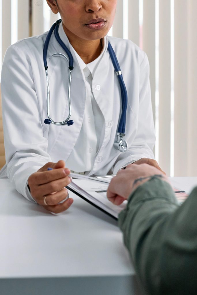 Ein Arzt im weißen Kittel berät einen Patienten an einem Tisch mit medizinischen Unterlagen.